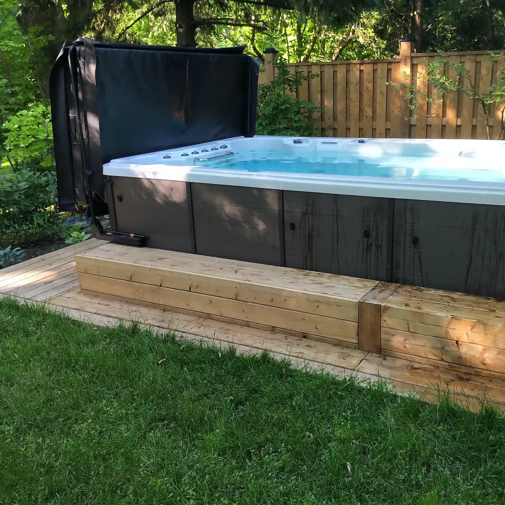 Canadian Spa Company St. Lawrence 13ft Swim Spa filled with no jets operating in a green garden setting with cover partially in view. 