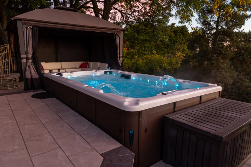 Canadian Spa Company St. Lawrence 13ft Swim Spa in dusky garden setting, showing blue LED lights and waterfall features in operation. 